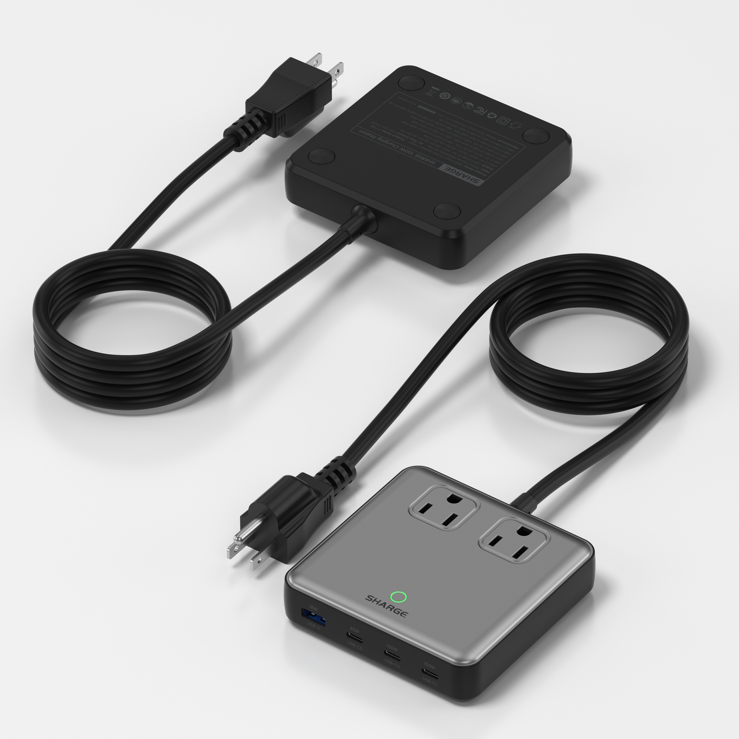 Top-down view of the Sharge 100W Charging Station showing two connected cables. One cable runs from a black rectangular power brick, and the other connects to a silver power module with two AC outlets and three USB ports on the front edge.