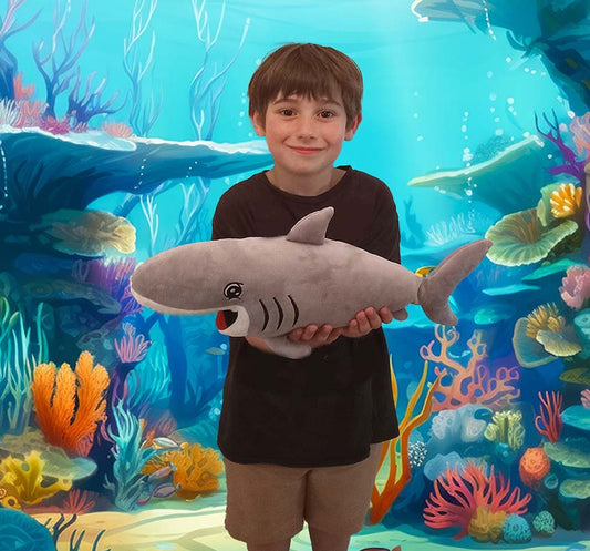 child in front of a mural of an underwater coral reef, holding up Ms. Finly shark. it is 18-inches long and smiles with an open mouth