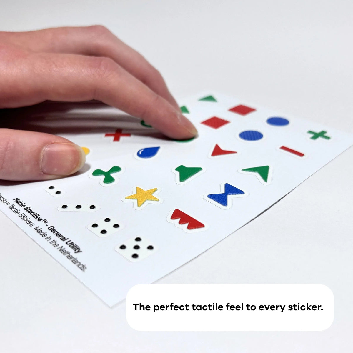 A hand feeling raised symbols on the Stactiles General Utility tactile sticker sheet.