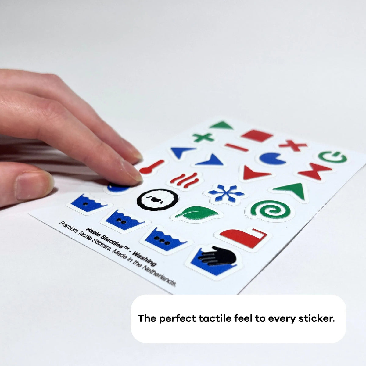 A hand feeling raised laundry symbols on the Stactiles Washing tactile sticker sheet.