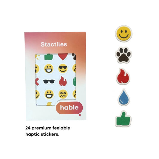 A composite image showcasing the Stactiles Emoji set. A circular inset in the top-left shows fingers exploring a sheet of colorful, raised emoji stickers. In the bottom-left, a classic yellow smiley face sticker is shown on a fingertip for scale. The main image features a sheet of 24 unique haptic stickers—including various facial expressions, a heart, a fire symbol, and a thumbs up—displayed next to the Hable retail packaging.